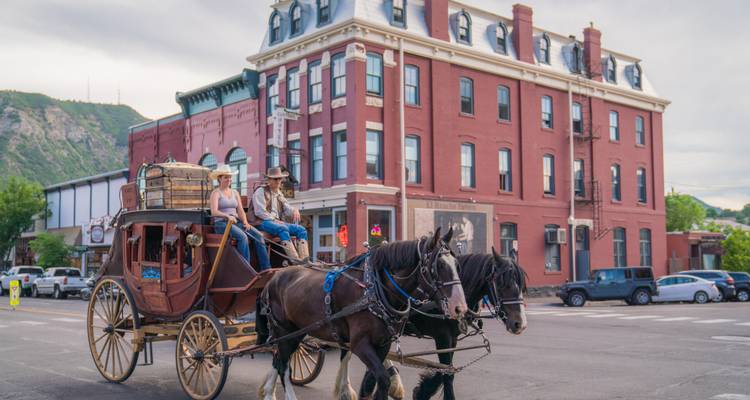 Calèche tirée par des chevaux passant devant un bâtiment historique en briques rouges.