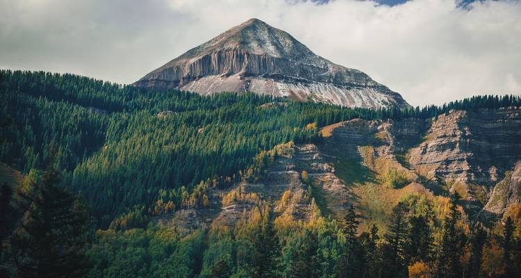 Sommet de montagne avec des arbres d'automne et un ciel nuageux.