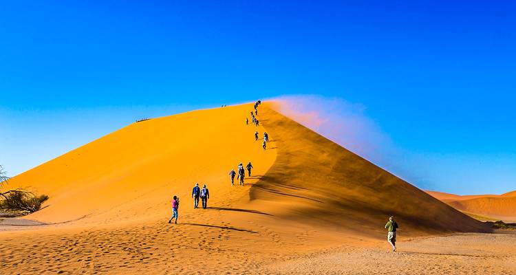 Grupo de personas haciendo senderismo por una duna de arena.