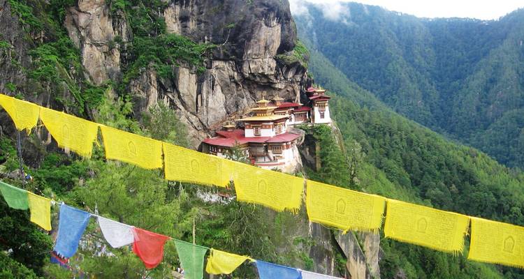 Complexe monastique sur une falaise avec des drapeaux de prière colorés au premier plan.