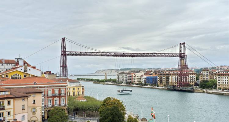 Puente de hierro sobre un río con edificios residenciales a ambos lados.