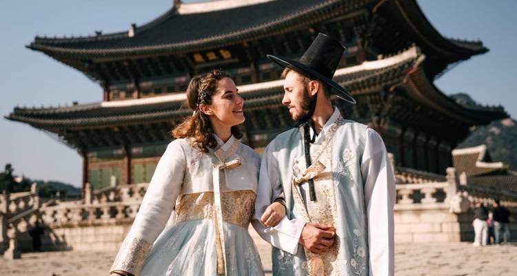 Couple en vêtements traditionnels coréens debout devant un bâtiment historique.