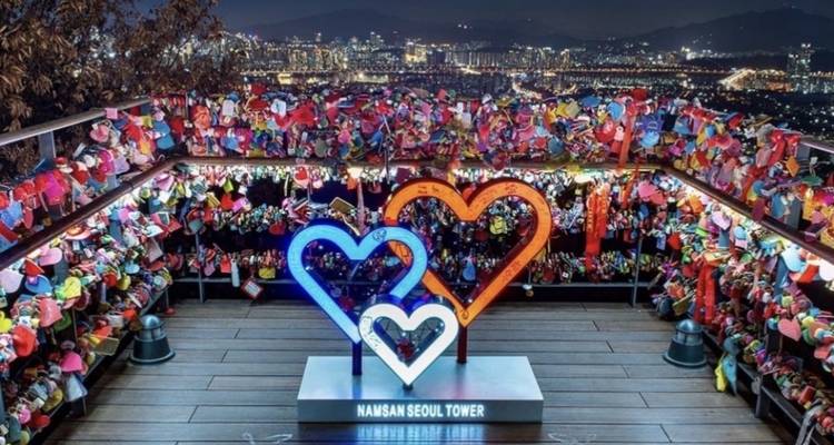 Des cadenas colorés entourent une installation sur le thème de l'amour surplombant un paysage urbain la nuit.