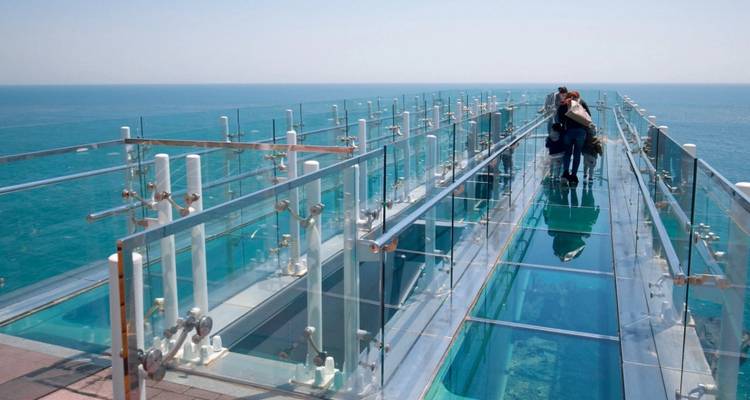 Des personnes marchant sur une passerelle en verre au-dessus de l'océan.