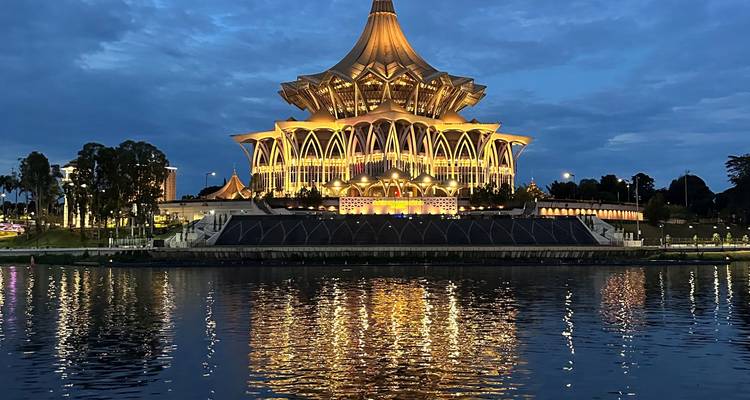 Elegantes Flussgebäude, das bei Einbruch der Dämmerung in goldenem Licht erstrahlt, gespiegelt auf ruhigem Wasser.