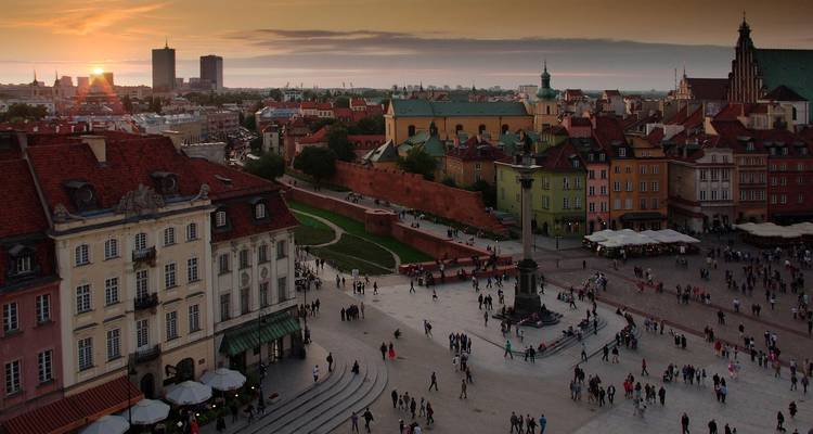Place de ville animée au coucher du soleil avec des bâtiments historiques, des gens et un horizon.
