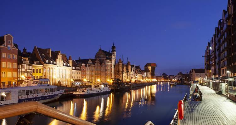 Photo de soirée d'un canal urbain avec des bâtiments historiques illuminés et des bateaux.