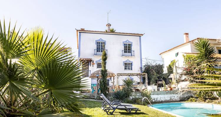 Maison blanche à deux étages avec un jardin et une piscine sous un ciel dégagé.