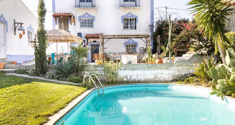 Vue de jardin avec une piscine et une maison blanche entourée de verdure.