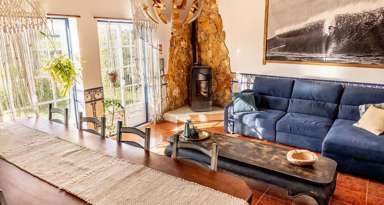 Salon avec une table à manger, un canapé bleu, une cheminée et de grandes fenêtres.