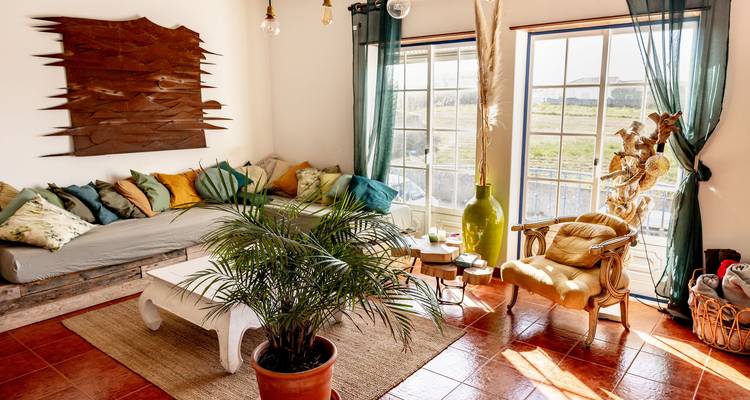 Salon lumineux avec canapés, plantes et grandes fenêtres.