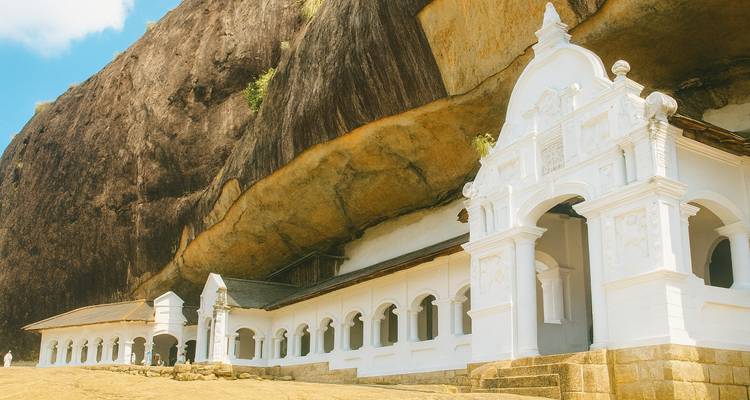 Weiße Fassade eines historischen Tempels, der gegen einen Felsen gebaut wurde.