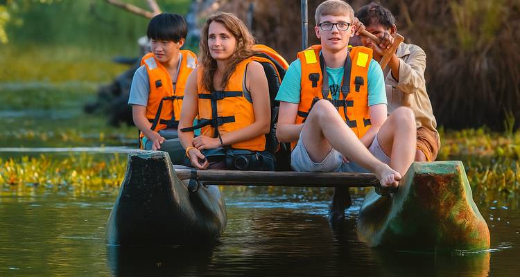 Drei Touristen mit Schwimmwesten sitzen in einem Boot auf einem ruhigen Gewässer.