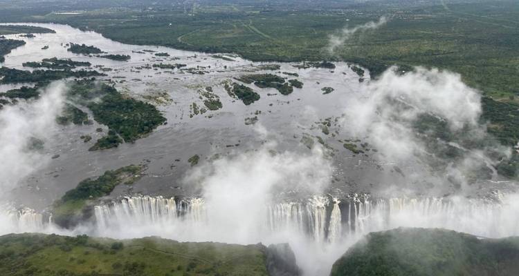 Vue aérienne des chutes Victoria avec la brume qui s'élève et une végétation luxuriante environnante.