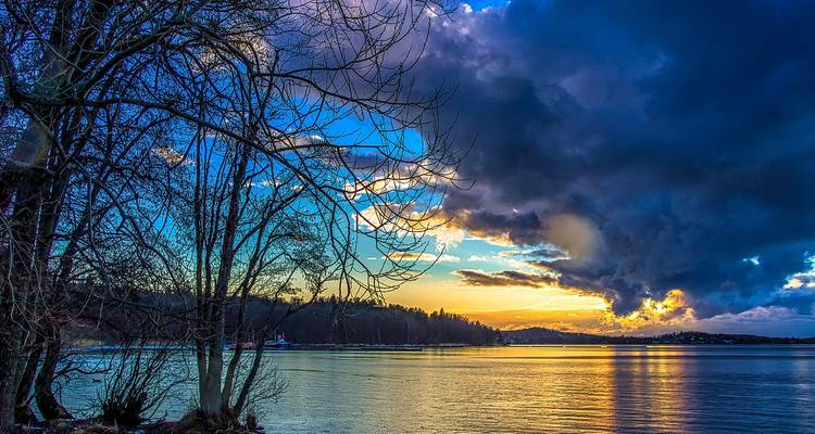 Ciel dramatique au-dessus d'un lac calme avec des arbres et des rives lointaines.