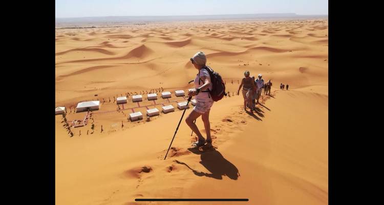 Groupe de personnes escaladant une dune avec un camp du désert en contrebas.