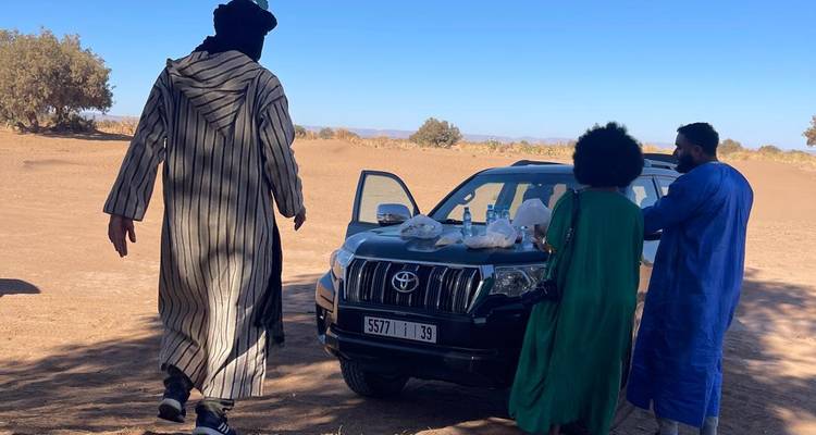 Trois personnes debout près d'une voiture avec un arrière-plan désertique.