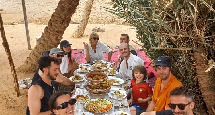 Groupe de personnes savourant un repas en plein air sous des palmiers.