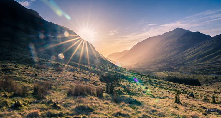 Sunrise over a lush valley with mountains in the distance.
