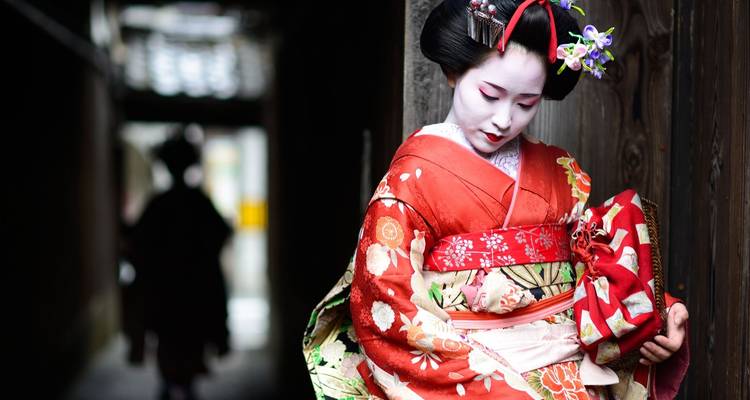Geisha en tenue traditionnelle appuyée contre un mur de bois