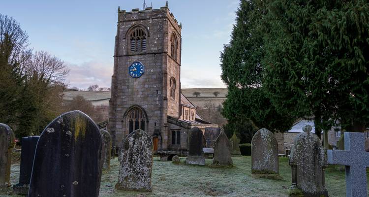 Antigua iglesia de piedra con un cementerio en un entorno rural.
