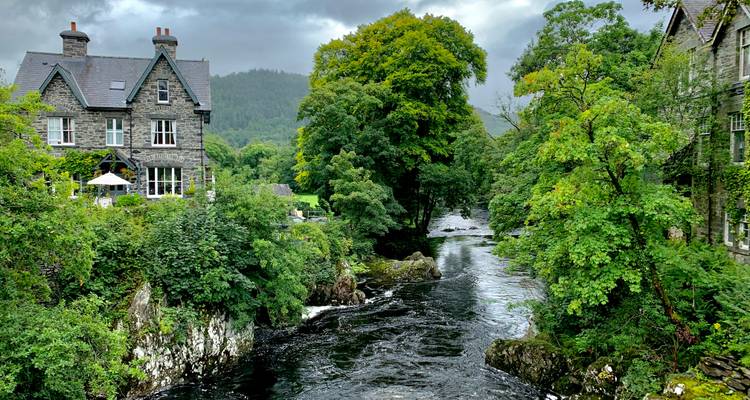 Charmantes Dorf mit Steinhäusern und einem Fluss, umgeben von üppigem Grün.