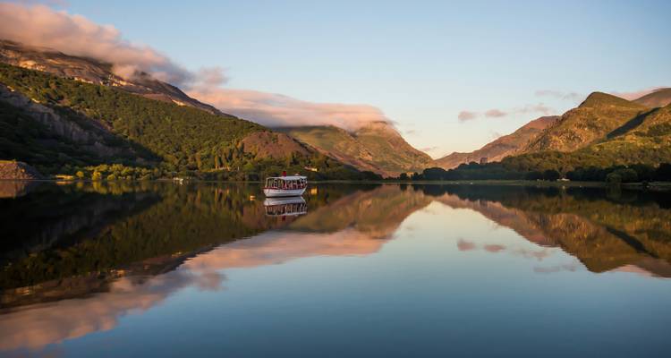 Ruhiger See umgeben von Bergen mit einem Boot auf dem Wasser.