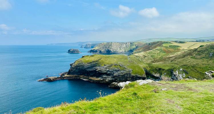 Falaises côtières spectaculaires avec un océan bleu clair et des champs verts.