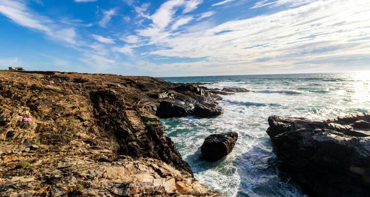 Côte escarpée avec des vagues qui se brisent contre les rochers sous un ciel bleu.