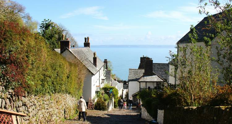 Rue de village pittoresque menant à la mer avec un chemin pavé et des maisons.