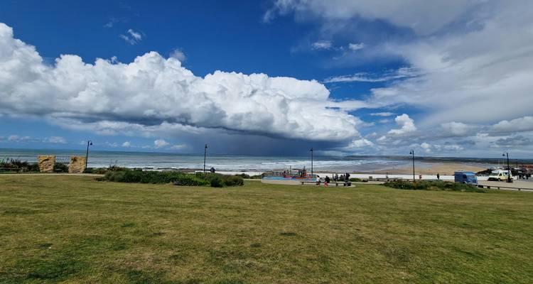 Ciel nuageux au-dessus d'une plage avec des gens qui marchent sur une zone herbeuse.