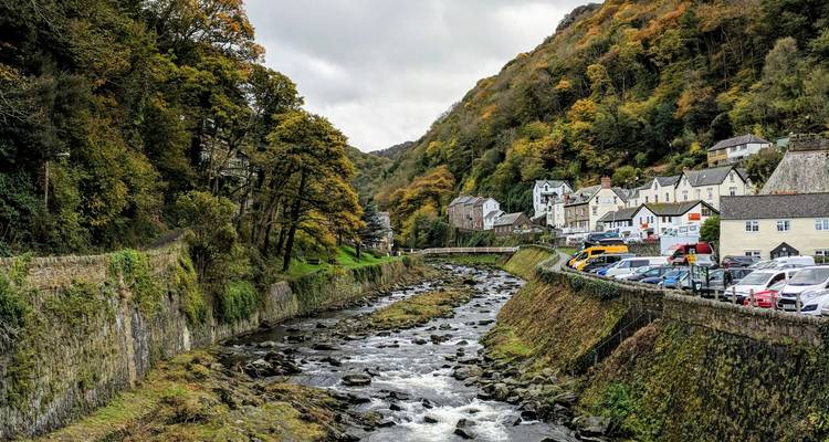 Rivière qui traverse une vallée avec des maisons d'un côté et un feuillage d'automne.