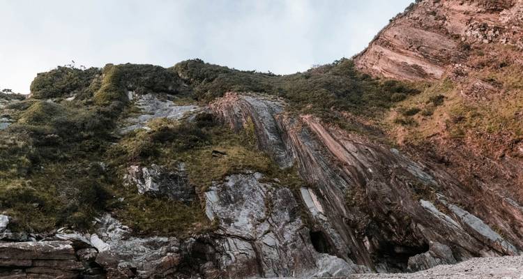 Falaise rocheuse avec végétation verte contre le ciel.