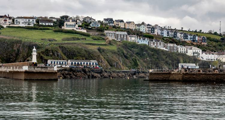 Vue de bateaux de pêche dans un port avec un phare en arrière-plan.