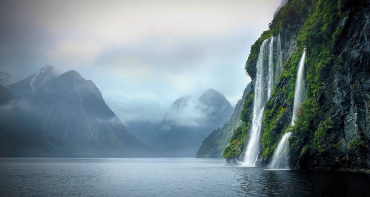 Des cascades dévalant des falaises dans un fjord sous un ciel brumeux.