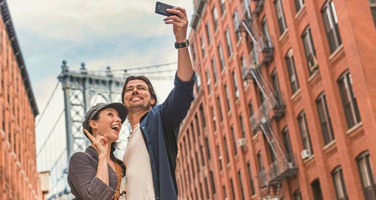 Ein Paar macht ein Selfie vor einer Brücke in New York City.