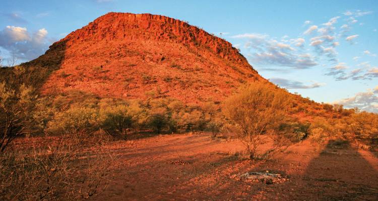 Montagne rouge escarpée sous un soleil couchant.