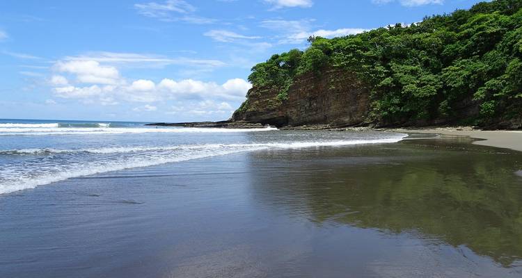 Strand met golven en een rotsachtige klif in de verte.