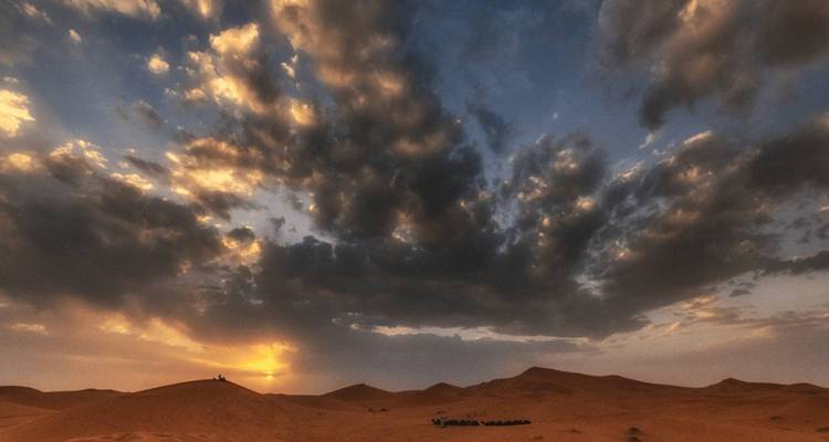 Atardecer sobre paisaje desértico con nubes dramáticas.