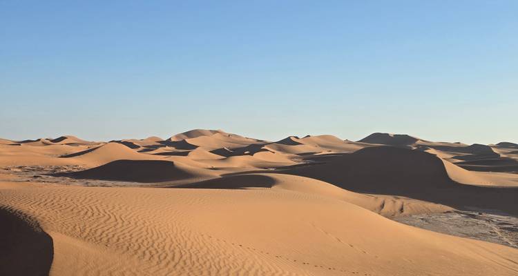 Weids daglicht uitzicht van eindeloze glooiende zandduinen onder een heldere bleekblauwe hemel.