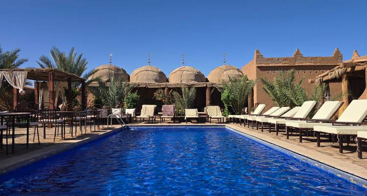 Uitnodigende hotelzwembad omlijst door ligstoelen en adobe koepelkamers tegen een heldere woestijnlucht.