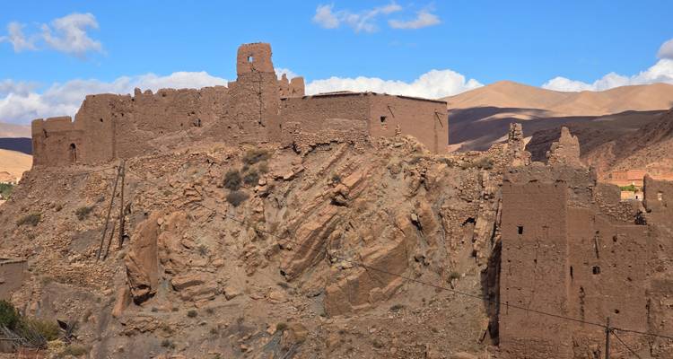 Ruwe ruïnes van een oude kasbah gelegen op een rotsachtige heuvelflank onder een blauwe hemel.