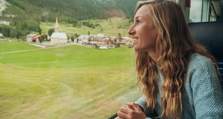 Vrouw die vanuit een treinraam naar een pittoresk dorpje kijkt.