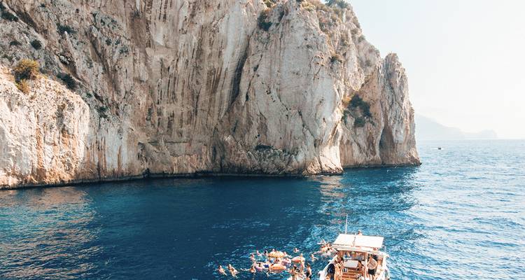 Los nadadores disfrutan del agua azul cristalina junto a imponentes acantilados de piedra caliza mientras un barco ancla cerca de Capri.