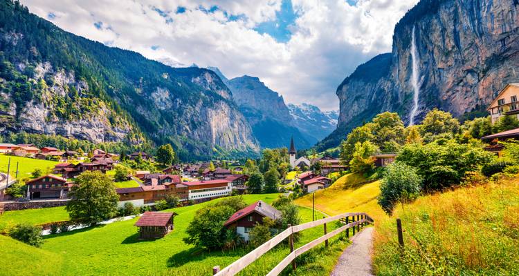 Malerisches Dorf mit Wasserfall und Bergen im Hintergrund.