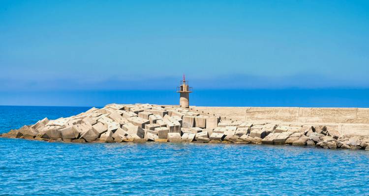 Mer avec un phare sur un brise-lames sous un ciel dégagé.