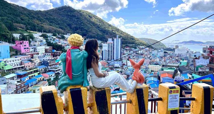 Vue panoramique de bâtiments colorés avec une personne et une statue assises sur un mur.