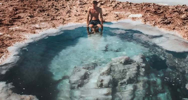 Personne agenouillée près d'un petit bassin limpide avec des formations rocheuses.