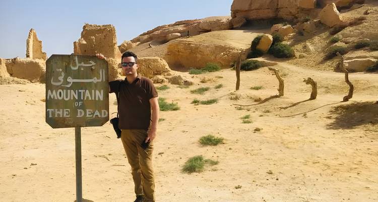 Personne posant avec un panneau indiquant 'Montagne des Morts' dans un désert.