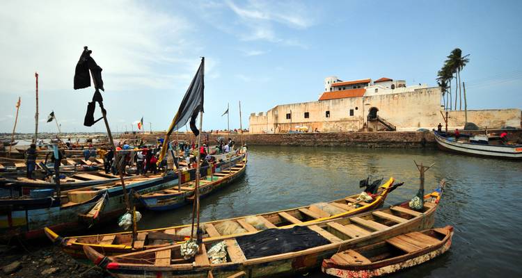 Boats in a harbor beside a historic fort under a clear sky.